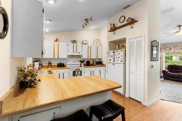 kitchen with white appliances, vaulted ceiling, light hardwood / wood-style floors, white cabinets, and kitchen peninsula