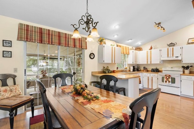 dining area with light hardwood / wood-style floors, a chandelier, sink, and vaulted ceiling