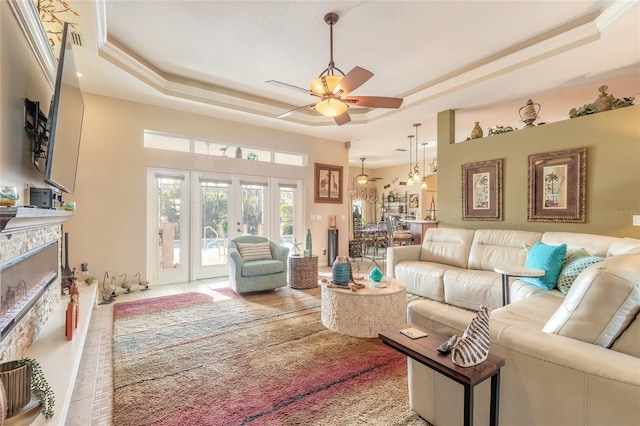 living room with ceiling fan, a stone fireplace, french doors, and a tray ceiling