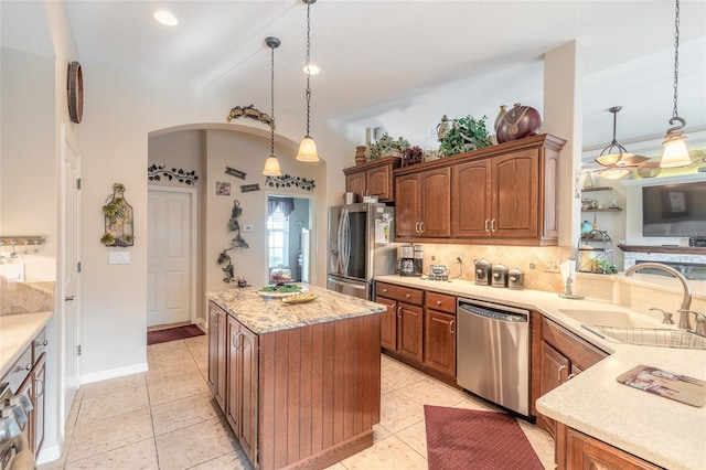 kitchen with stainless steel appliances, sink, light tile patterned floors, a center island, and hanging light fixtures