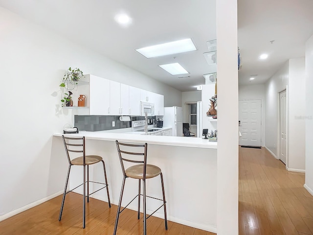 kitchen with light hardwood / wood-style floors, white cabinetry, kitchen peninsula, a breakfast bar area, and white appliances