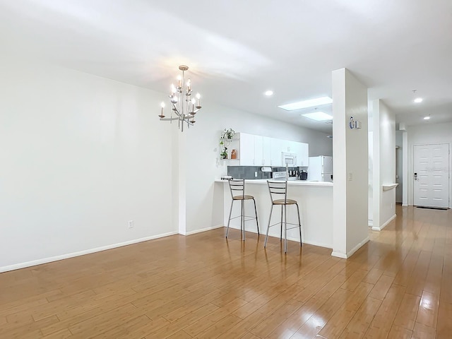 kitchen with a kitchen bar, light hardwood / wood-style floors, white cabinets, kitchen peninsula, and white appliances