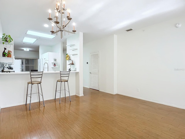 kitchen featuring white fridge, light wood-type flooring, an inviting chandelier, white cabinets, and kitchen peninsula