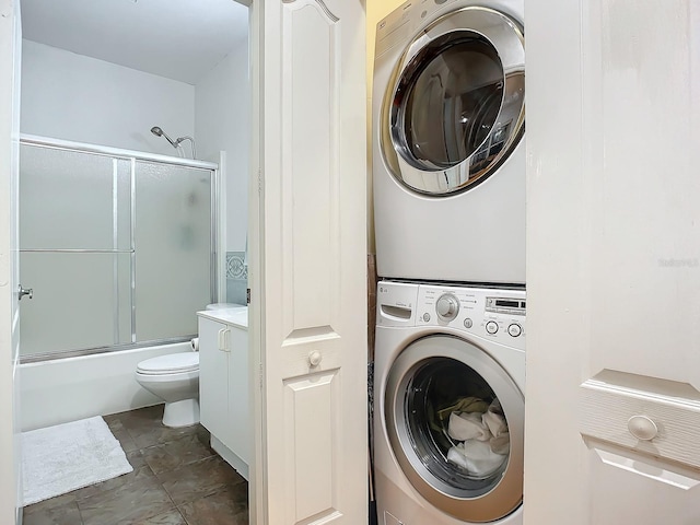 clothes washing area featuring dark tile patterned flooring and stacked washer and clothes dryer