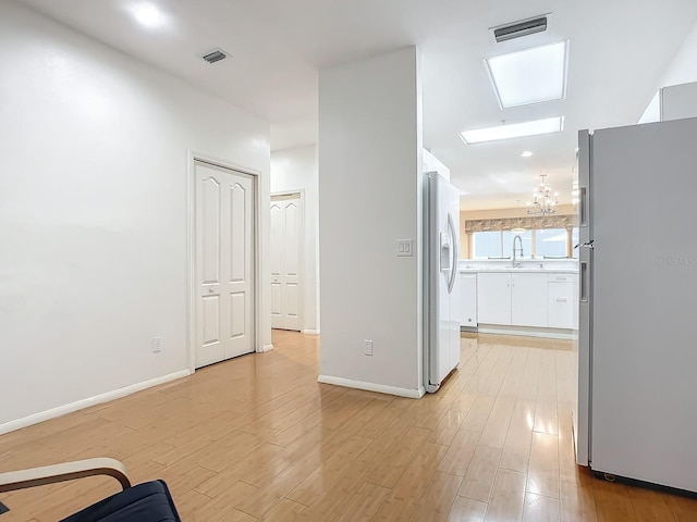 hall featuring light wood-type flooring, a notable chandelier, and sink