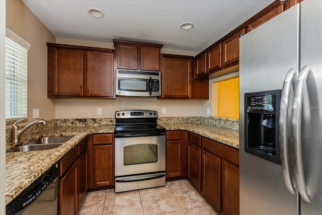 kitchen featuring a textured ceiling, sink, light stone counters, and stainless steel appliances