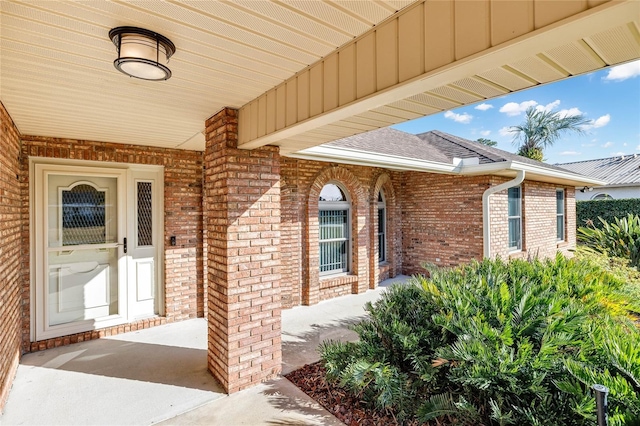 doorway to property with a patio, brick siding, and a shingled roof