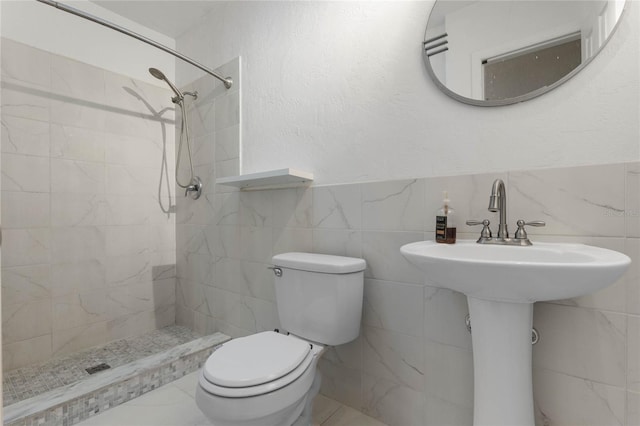 bathroom featuring a tile shower, sink, tile walls, and toilet