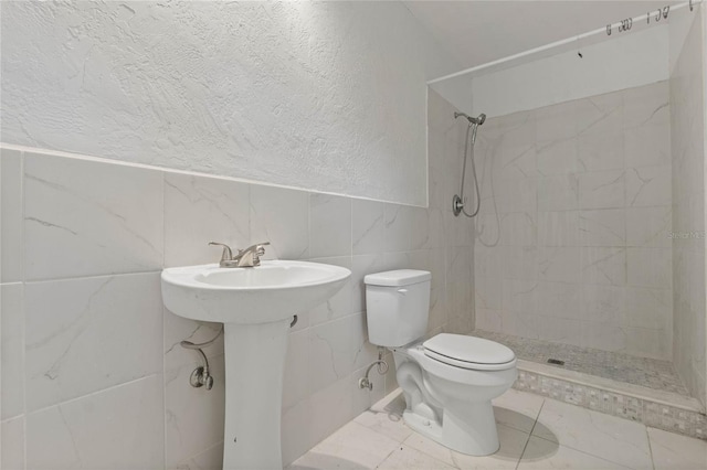 bathroom featuring sink, toilet, tile walls, and a tile shower