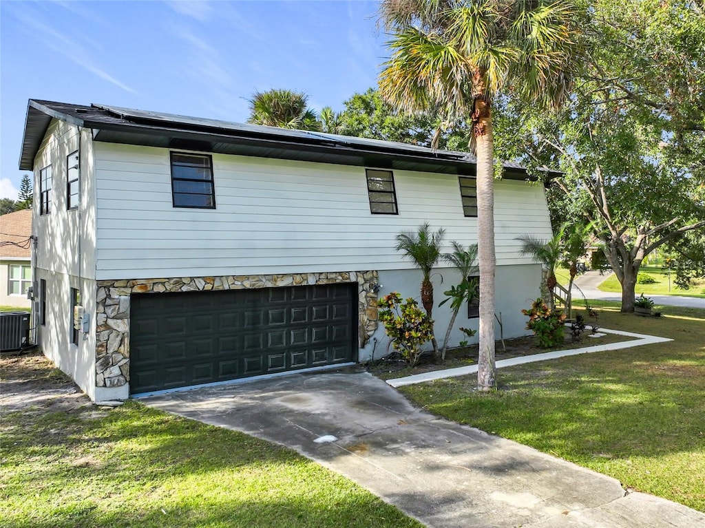 view of front of property featuring a front lawn, central air condition unit, and a garage