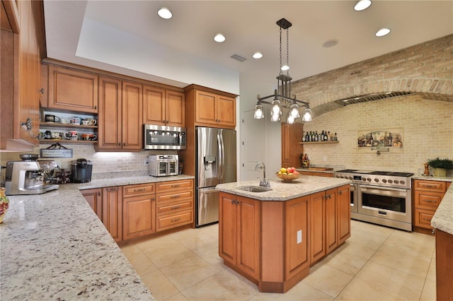 kitchen featuring light stone counters, appliances with stainless steel finishes, pendant lighting, sink, and a kitchen island with sink