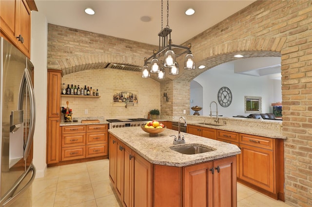 kitchen with an island with sink, stainless steel refrigerator, brick wall, and sink