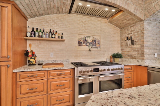 kitchen featuring stainless steel appliances, light stone counters, wall chimney range hood, and vaulted ceiling