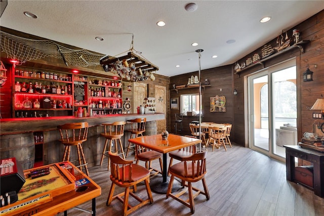 dining area with bar area, wooden walls, hardwood / wood-style floors, and a textured ceiling