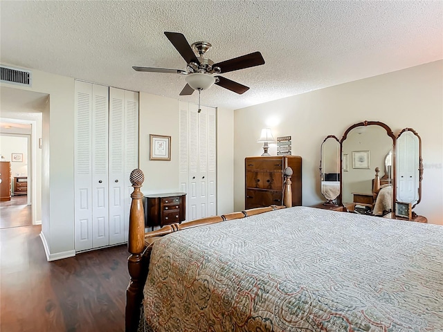 bedroom with dark hardwood / wood-style flooring, a textured ceiling, two closets, and ceiling fan