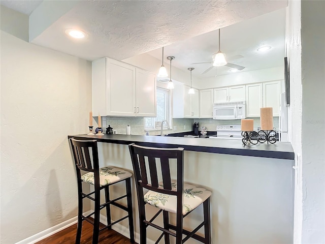 kitchen featuring white cabinetry, ceiling fan, a breakfast bar area, dark hardwood / wood-style floors, and white appliances