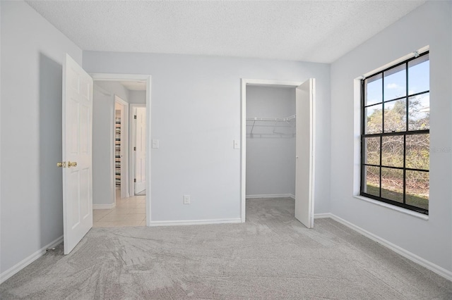 unfurnished bedroom with light colored carpet, a walk in closet, a textured ceiling, and a closet