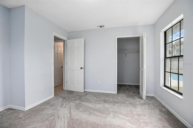 unfurnished bedroom with light carpet, a closet, a spacious closet, and multiple windows