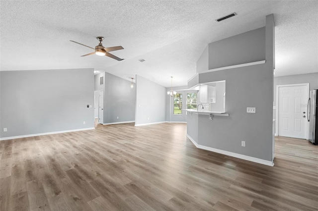 unfurnished living room featuring a textured ceiling, hardwood / wood-style floors, vaulted ceiling, and ceiling fan with notable chandelier