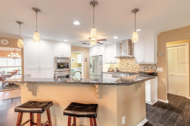 kitchen featuring appliances with stainless steel finishes, a kitchen bar, white cabinets, wall chimney range hood, and dark hardwood / wood-style flooring