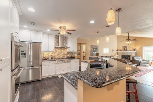 kitchen with stainless steel appliances, sink, vaulted ceiling, white cabinets, and wall chimney exhaust hood