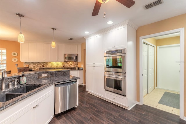 kitchen with stainless steel appliances, dark wood-type flooring, sink, white cabinets, and pendant lighting