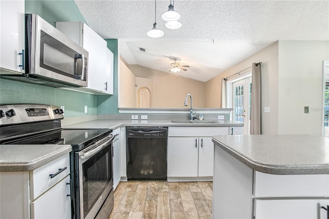 kitchen with pendant lighting, lofted ceiling, sink, white cabinetry, and stainless steel appliances