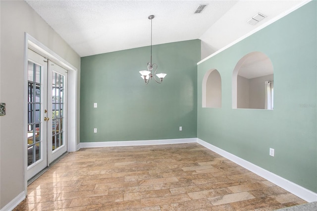 unfurnished room with french doors, an inviting chandelier, light hardwood / wood-style floors, a textured ceiling, and lofted ceiling