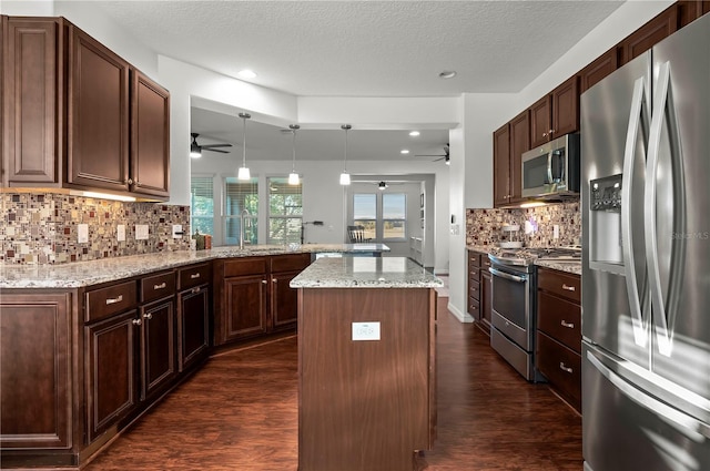 kitchen with dark hardwood / wood-style floors, kitchen peninsula, pendant lighting, a kitchen island, and appliances with stainless steel finishes