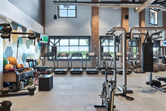 gym with a towering ceiling, plenty of natural light, and brick wall