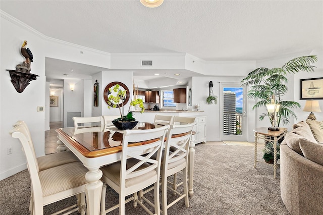 dining room featuring light colored carpet, a textured ceiling, and ornamental molding