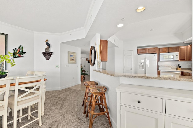 kitchen featuring light stone counters, white appliances, light colored carpet, and crown molding