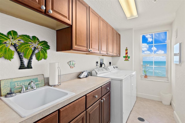 laundry area featuring light tile patterned flooring, washer and clothes dryer, cabinets, sink, and a water view