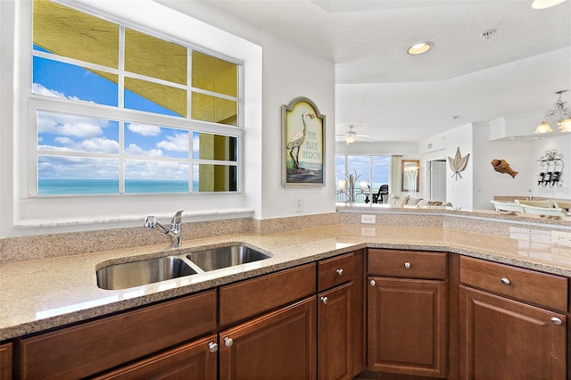 kitchen with a water view, sink, light stone counters, and a textured ceiling