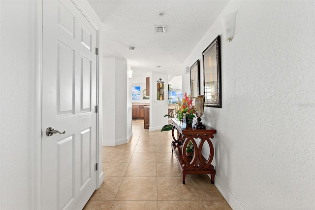 corridor featuring a textured ceiling and light tile patterned floors