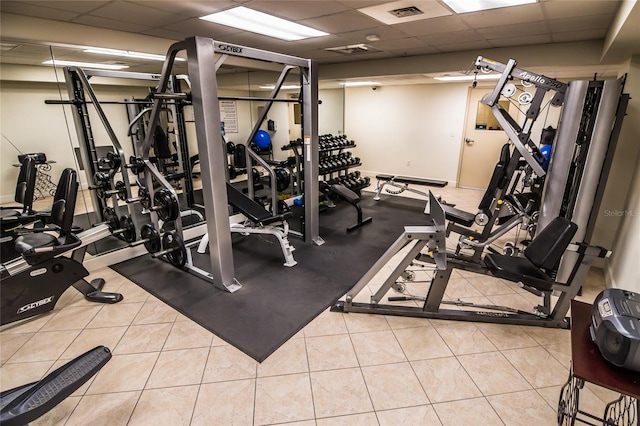 workout area featuring a drop ceiling and light tile patterned flooring