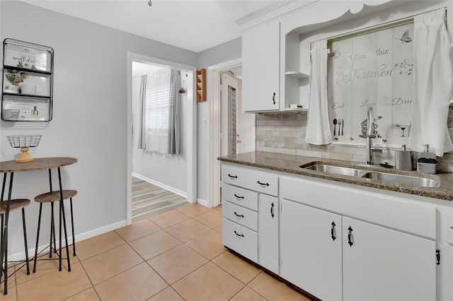 kitchen featuring sink, white cabinetry, light tile patterned flooring, decorative backsplash, and dark stone counters