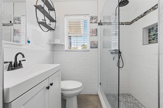 bathroom featuring tile patterned floors, vanity, tiled shower, tile walls, and toilet