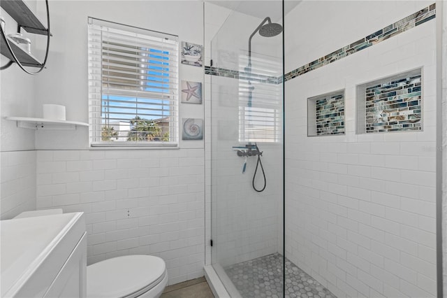 bathroom with a tile shower, vanity, tile walls, and toilet