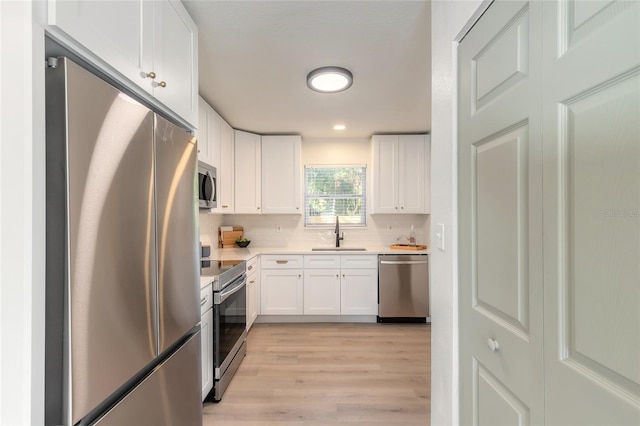 kitchen with appliances with stainless steel finishes, tasteful backsplash, sink, white cabinets, and light hardwood / wood-style floors