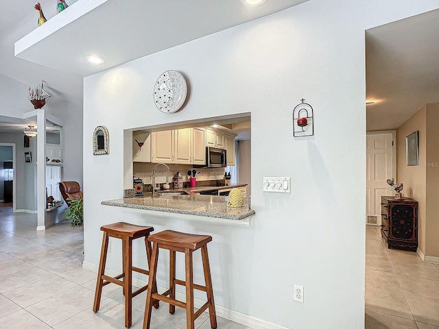 kitchen featuring kitchen peninsula, light stone counters, a breakfast bar, sink, and light tile patterned flooring