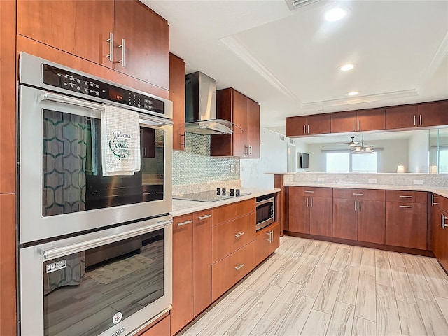 kitchen with a raised ceiling, light hardwood / wood-style flooring, wall chimney exhaust hood, decorative backsplash, and appliances with stainless steel finishes