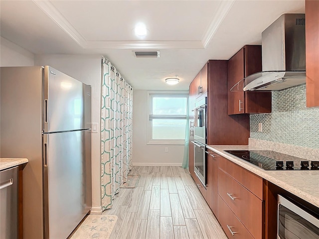 kitchen with light wood-type flooring, backsplash, wall chimney exhaust hood, stainless steel appliances, and a raised ceiling