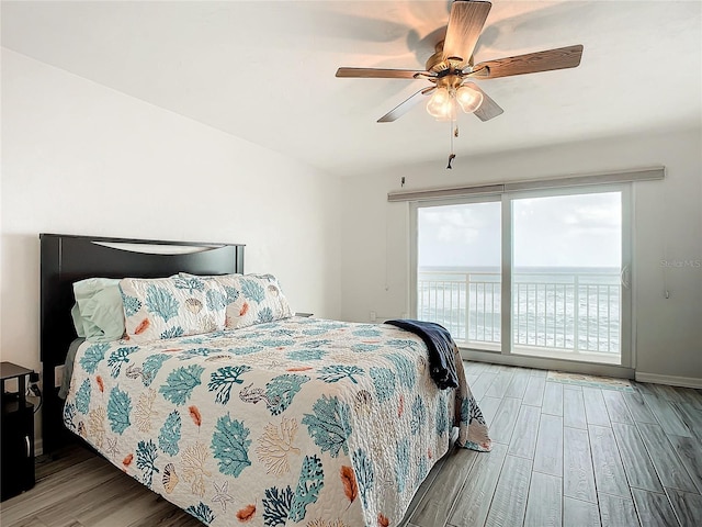 bedroom with access to outside, ceiling fan, a water view, and hardwood / wood-style flooring