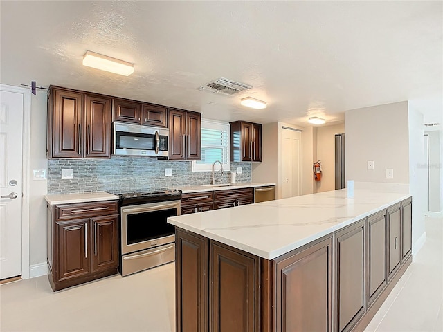 kitchen with kitchen peninsula, decorative backsplash, light stone counters, stainless steel appliances, and sink