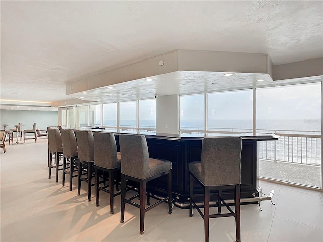 interior space featuring bar area, a water view, light tile patterned flooring, and a textured ceiling