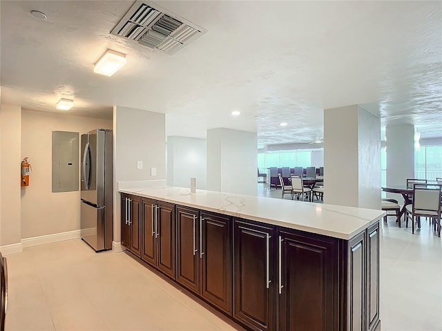 kitchen featuring kitchen peninsula, a textured ceiling, dark brown cabinetry, electric panel, and stainless steel refrigerator