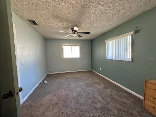 spare room featuring ceiling fan, dark carpet, and a textured ceiling