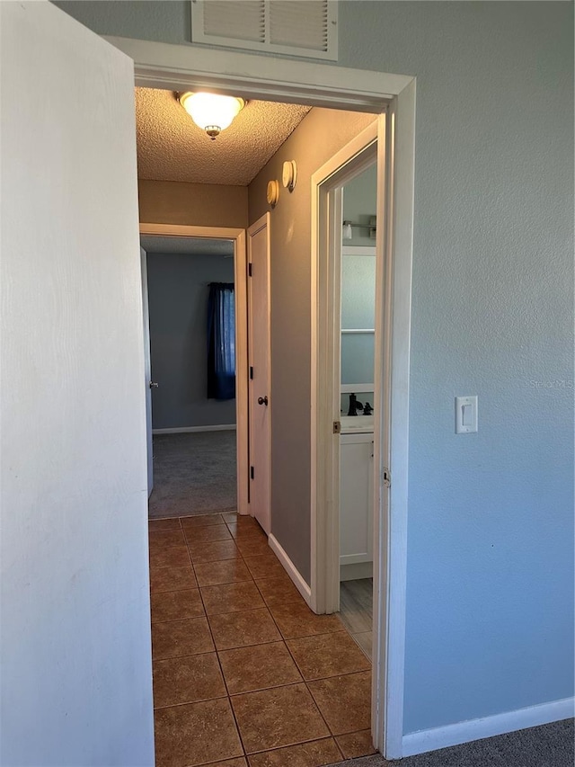 corridor featuring dark tile patterned floors and a textured ceiling