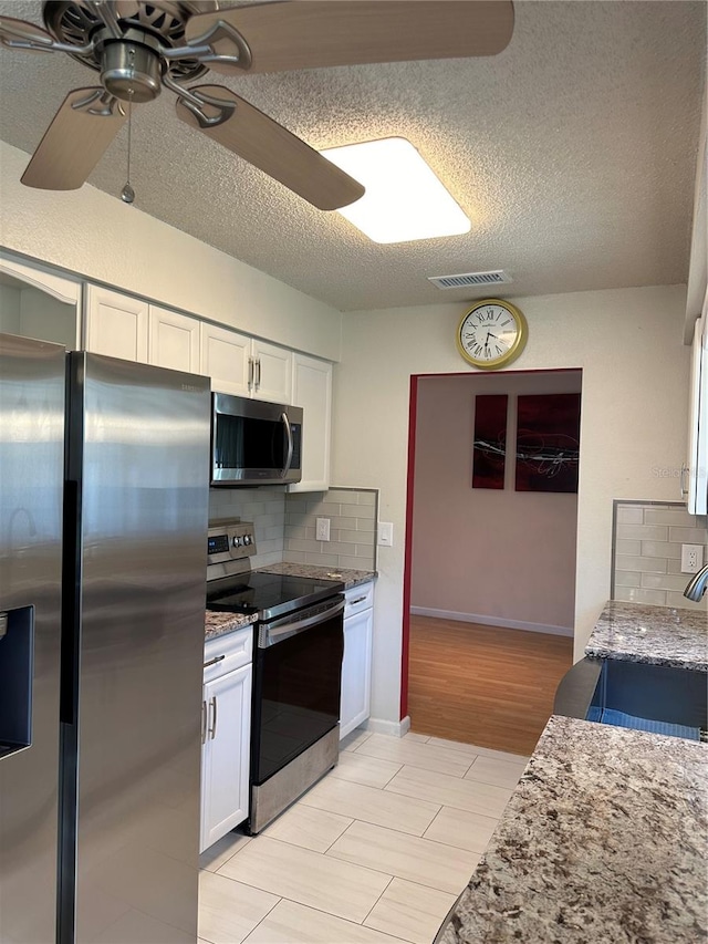 kitchen with white cabinets, decorative backsplash, ceiling fan, light stone counters, and stainless steel appliances